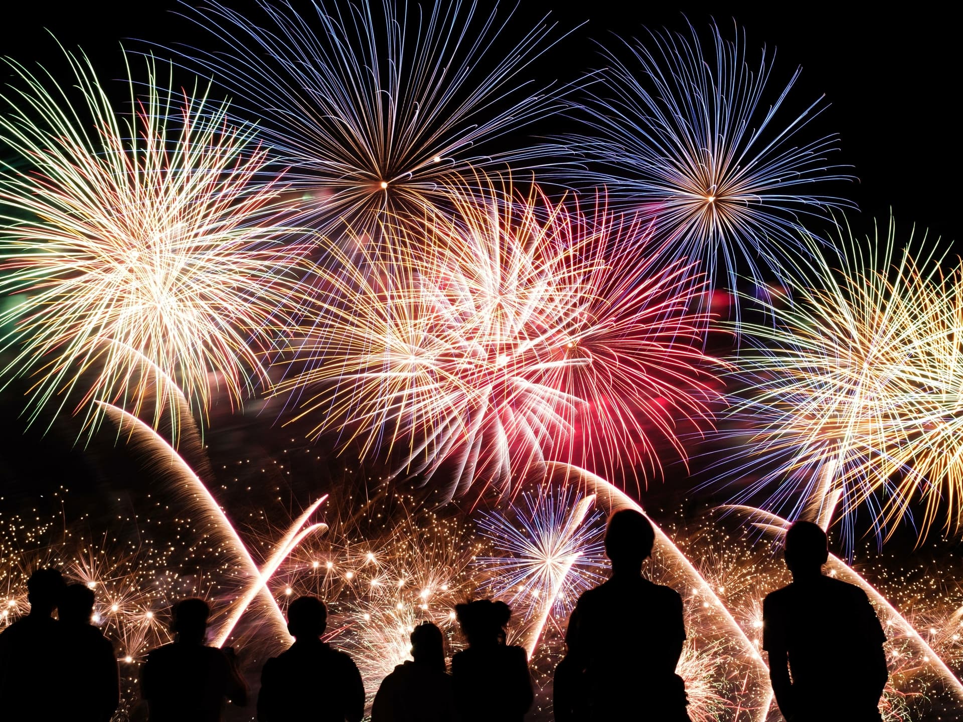Nine people watching multi coloured firework display